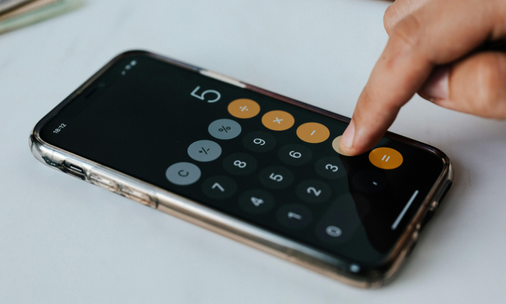 Mano usando la calculadora de un móvil para realizar cálculos financieros.