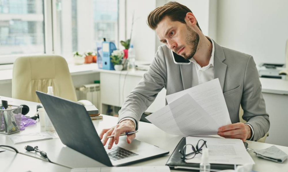 Hombre revisando documentos y hablando por teléfono mientras calcula una factura, representando el proceso de facturar sin ser autónomo.