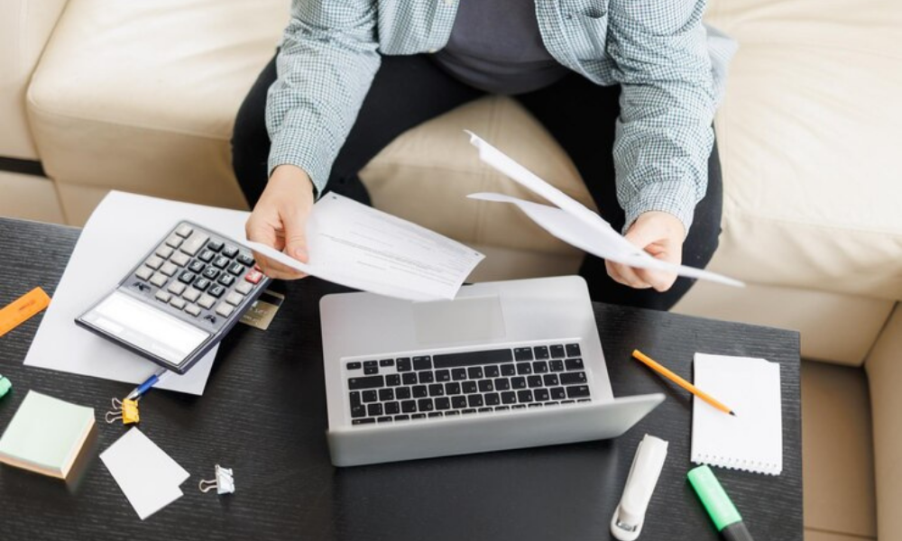 Persona revisando facturas y usando una calculadora en casa, ilustrando cómo hacer una factura sin ser autónomo.